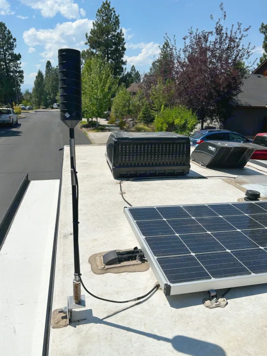 View of an RV rental roof featuring a Winegard antenna for connectivity, a solar panel, and AC units, set against a street.. R-Pod Hood River Edition 2020