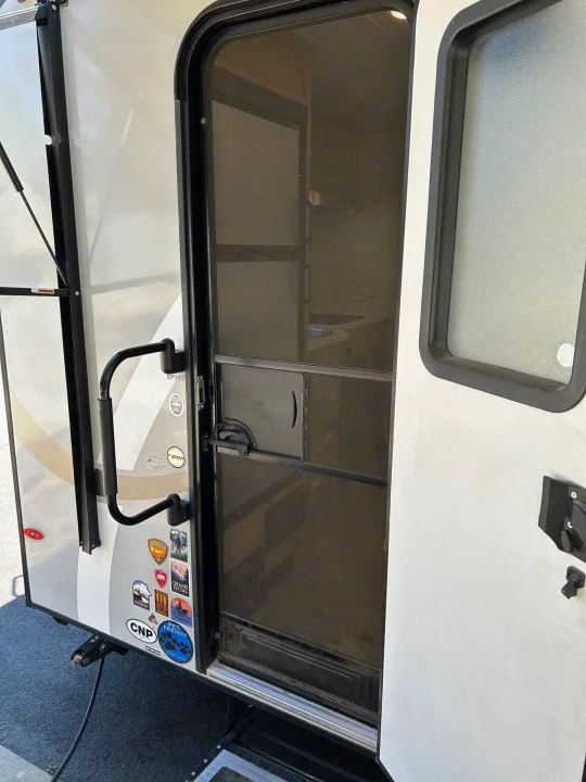 RV rental entrance: main door open, revealing a screen door. A black grab handle and travel stickers adorn the side.. R-Pod Hood River Edition 2020