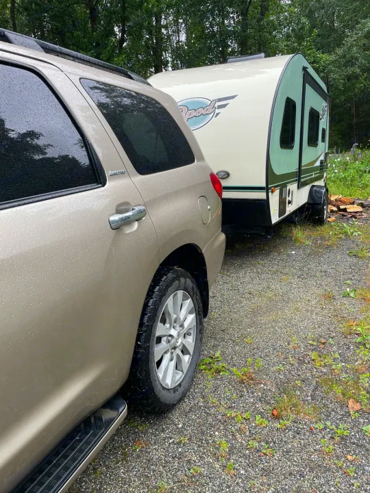 Rain-kissed tan Toyota Sequoia Limited SUV hitched to R-Pod rv rental. Gravel drive, lush trees imply adventure.. R-Pod R-Pod Trailer 2017