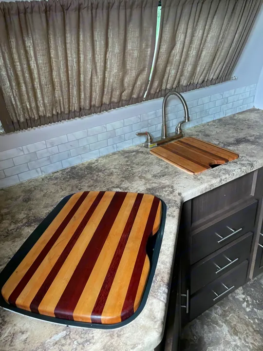 RV rental kitchen showing a sink, faucet, mottled countertops, and two wooden cutting boards. Light grey subway tile backsplash and brown curtains.. R-Pod R-Pod Trailer 2017