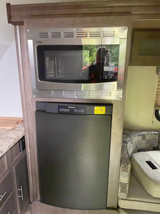 RV rental kitchen: stainless microwave over Dometic fridge in wood cabinetry, ideal for travel.. R-Pod R-Pod Trailer 2017