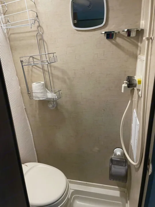 Inside an RV rental, a compact bathroom features a toilet, shower, mirror, and wall-mounted storage solutions.. R-Pod R-Pod Trailer 2017