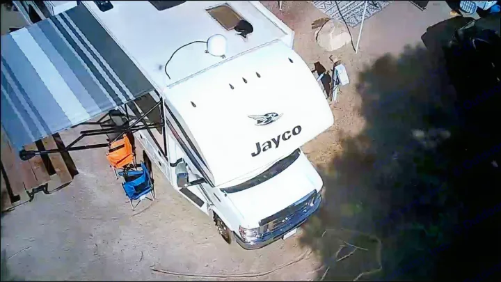 White Jayco RV rental shown from above, parked at a sunny campsite with an extended awning and colorful chairs.. Jayco Greyhawk 2018
