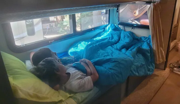 Cozy RV rental: Two kids comfortably tucked into a bunk, enjoying a movie, with another RV visible outside.. Jayco Greyhawk 2018