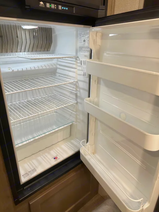 Open Norcold refrigerator and freezer in an RV rental, showing clean interior shelves, ready for your next adventure.. Venture Sonic Lite 2021