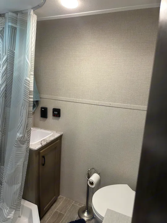 Clean RV rental bathroom showing shower, sink, toilet, and an RV control panel on the textured wall.. Venture Sonic Lite 2021