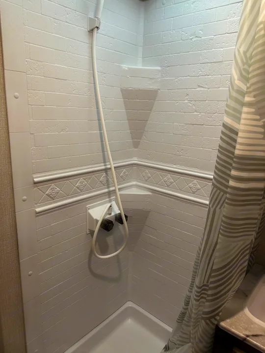 Compact rv rental shower: white faux brick walls, handheld shower, decorative trim, and a striped curtain.. Venture Sonic Lite 2021