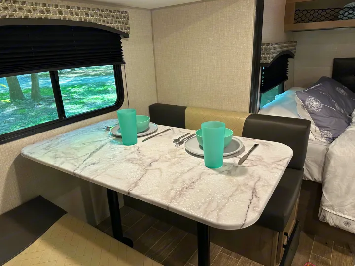 Cozy RV rental dinette with marble-look table and seating, ready for a meal with a view of nature. Bedroom area seen.. Venture Sonic Lite 2021