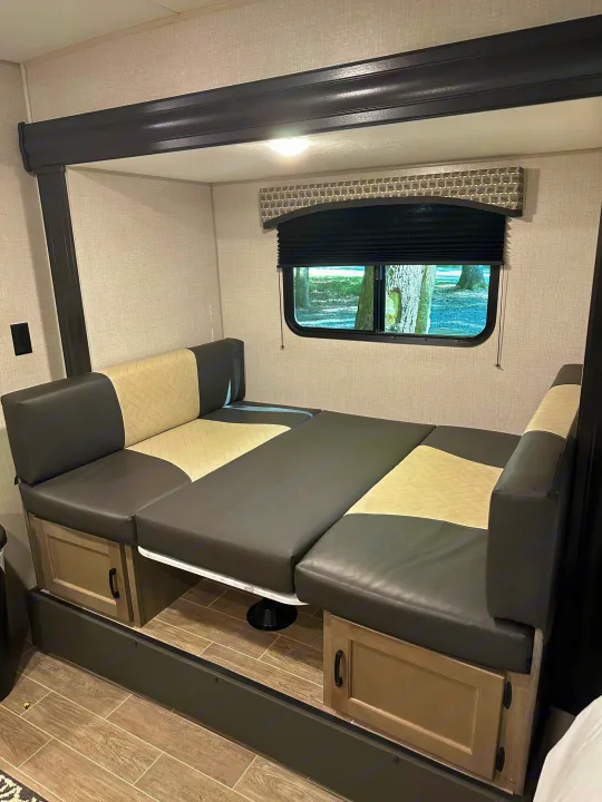 RV rental dinette transformed into a bed with two-tone cushions, featuring built-in storage and a window.. Venture Sonic Lite 2021