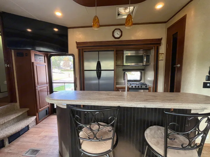 Modern RV rental kitchen with stainless steel appliances, breakfast bar, and TV, offering a comfortable space on the road.. Forest River XLR Thunderbolt Toy Hauler 2015