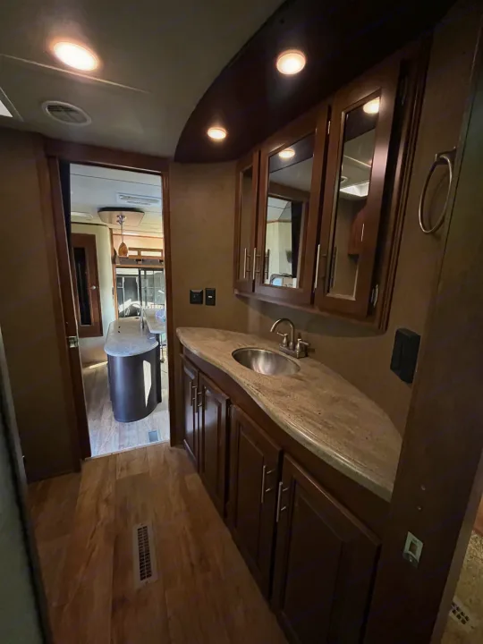Inside an RV rental, a well-lit vanity with a sink, mirrored cabinets, and wood floors, opening to the living/kitchen space.. Forest River XLR Thunderbolt Toy Hauler 2015