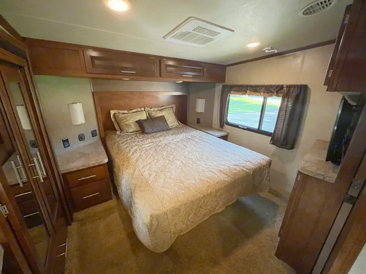 Spacious RV rental bedroom with a comfy bed, dark wood cabinets, a large window, and cozy lighting for restful travel.. Forest River XLR Thunderbolt Toy Hauler 2015