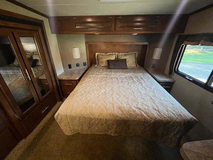 RV rental bedroom interior: large bed, wood headboard & cabinets, side tables, and mirrored closet. Ready for travel.. Forest River XLR Thunderbolt Toy Hauler 2015