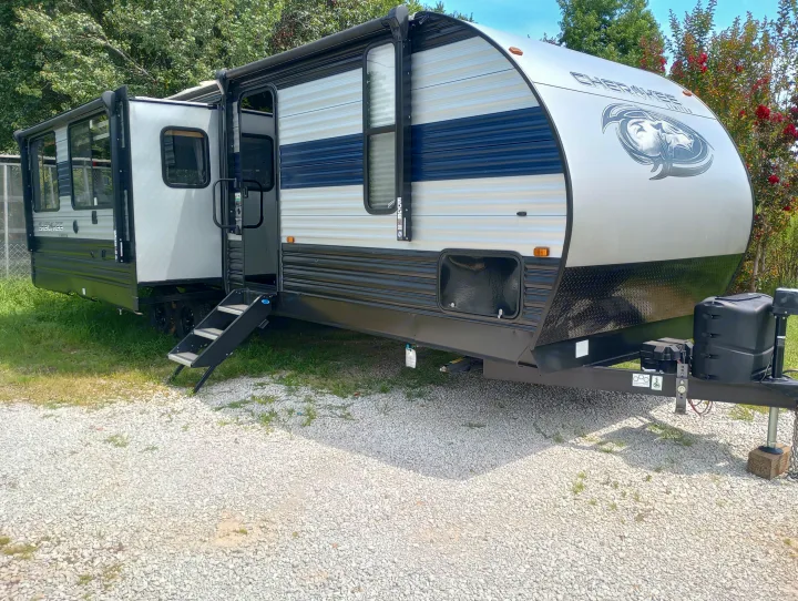 Spacious light gray RV rental (Cherokee Limited travel trailer) with blue stripe and steps, parked on gravel.. Forest River Cherokee 2022