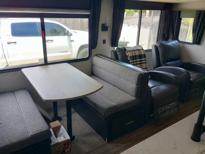 RV rental interior featuring a dinette with light wood table and grey bench seats, plus two black recliners.. Forest River Cherokee 2022