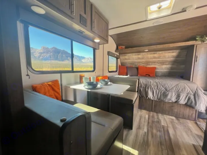 An RV rental interior features a dinette, bed, and large windows with desert mountain views, offering a comfortable travel space.. Riverside Retro 190BH 2023