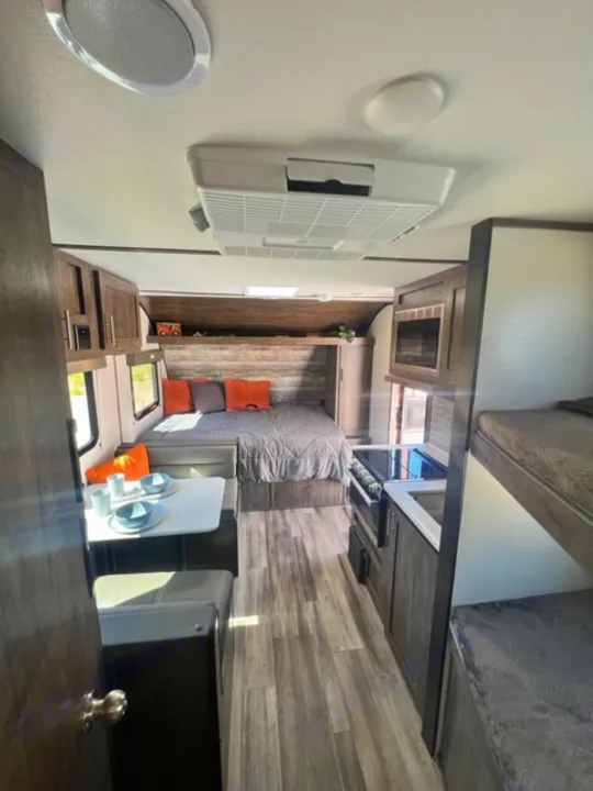 Spacious RV rental interior: modern bedroom, living/dining area, and kitchen. Light wood-look flooring throughout.. Riverside Retro 190BH 2023