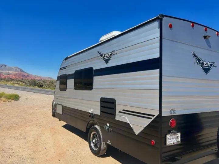 This silver and black RV rental, a travel trailer, is parked on a desert road shoulder with vibrant red mountains in the background.. Riverside Retro 190BH 2023