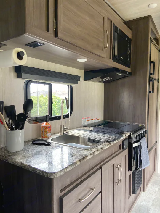 Compact RV rental kitchen with sink, stove, microwave, and ample storage, ready for travel adventures.. Genesis Supreme Rv Genesis Supreme 2022
