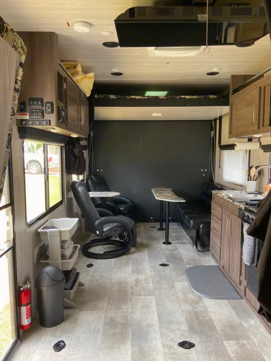 Interior of an RV rental, featuring a kitchen, seating, and overhead bunk. The floor has multiple tie-downs.. Genesis Supreme Rv Genesis Supreme 2022