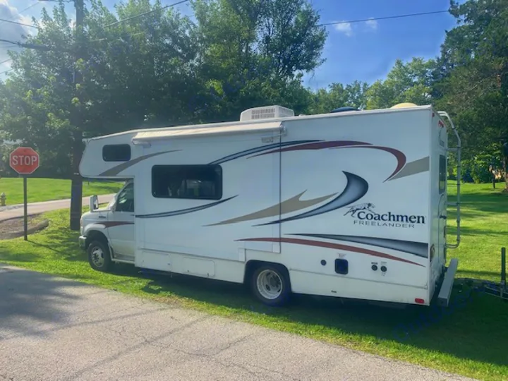 White Coachmen Freelander RV rental, with brown/grey stripes and windows, parked on grass beside a road.. Other Other 2014