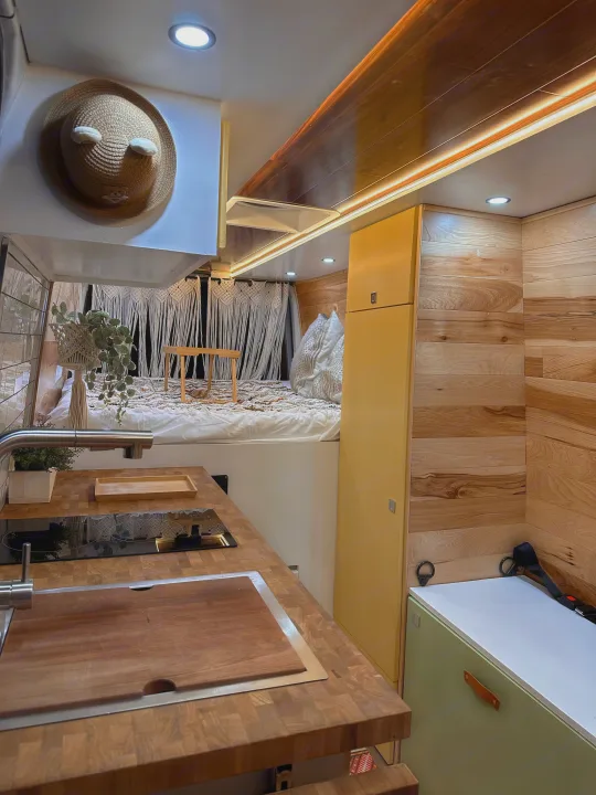 This RV rental interior features a modern kitchen, wooden countertops, cozy bed, and warm wood paneling.. Mercedes-Benz Sprinter 2022