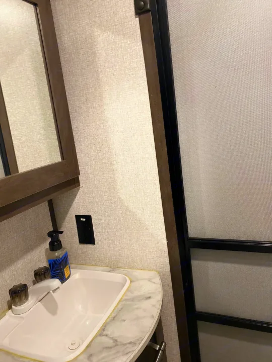 Inside an RV rental: a compact bathroom featuring a white sink, marble-look counter, mirrored cabinet, and screen door, perfect for travel.. Coleman Lantern 2021