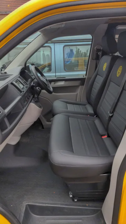 Shows the clean interior of a yellow Volkswagen van, featuring black seats with yellow VW logos. Perfect for an RV rental.. Volkswagen T6 2017