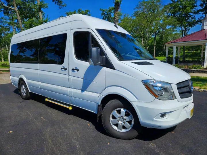 White Mercedes Sprinter van, often an RV rental, parked on asphalt with sunlit trees & gazebo background for travel.. Mercedes-Benz Sprinter 2017