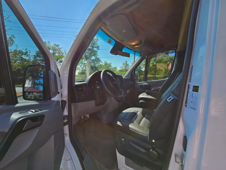 Interior of a white RV rental van, showing driver's seat, steering wheel, and dash. Trees visible outside.. Mercedes-Benz Sprinter 2017