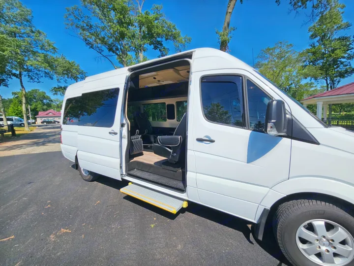 Spacious white RV rental van with open door, revealing a plush interior with captain's chairs and wood floor. Ready for travel.. Mercedes-Benz Sprinter 2017