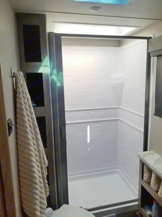 Clean RV rental bathroom with a bright, white, brick-patterned shower, glass door, and towel hooks.. Grand Design Imagine XLS 2021