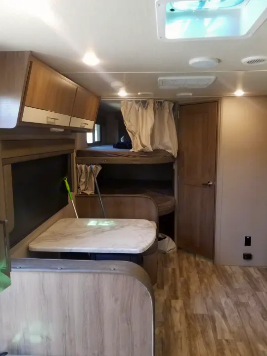 An RV rental interior with a bright dinette, overhead storage, and private bunk beds, ideal for travel comfort.. Grand Design Imagine XLS 2021