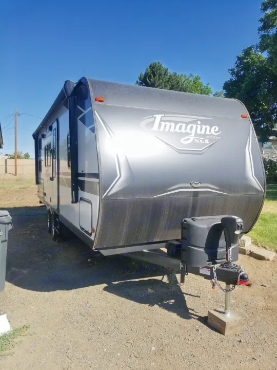 Sleek Grand Design Imagine XLS travel trailer, perfect for an RV rental getaway. Parked on gravel under a clear blue sky.. Grand Design Imagine XLS 2021