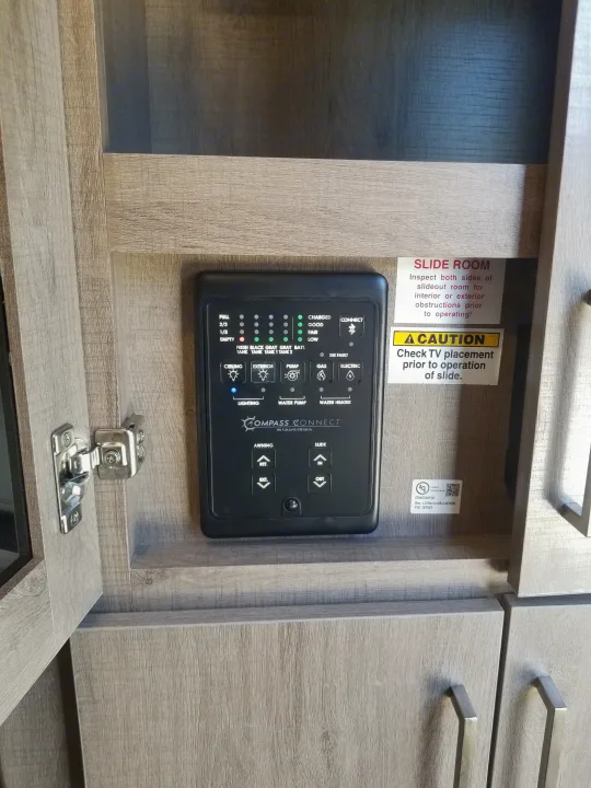 RV rental interior: A Compass Connect panel controls tank levels, battery, lights, water, awning, and slide-out. Important warnings for slide room operation are visible.. Grand Design Imagine XLS 2021