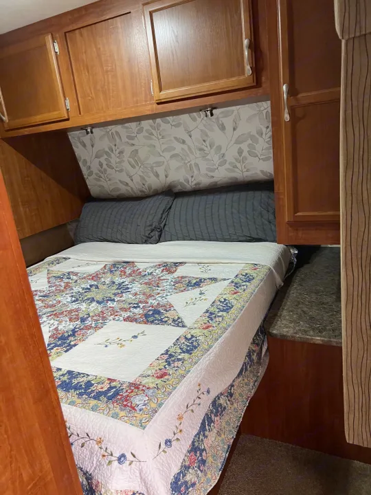 Cozy RV rental bedroom featuring a colorful quilt on the bed, grey pillows, and wooden overhead storage cabinets.. Jayco Camper Trailer- Eagle 2011