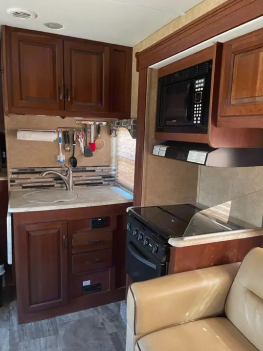 RV rental interior: A modern kitchen area with a microwave, stove, sink, and adjacent tan sofa.. Forest River Forester 317DS 2014