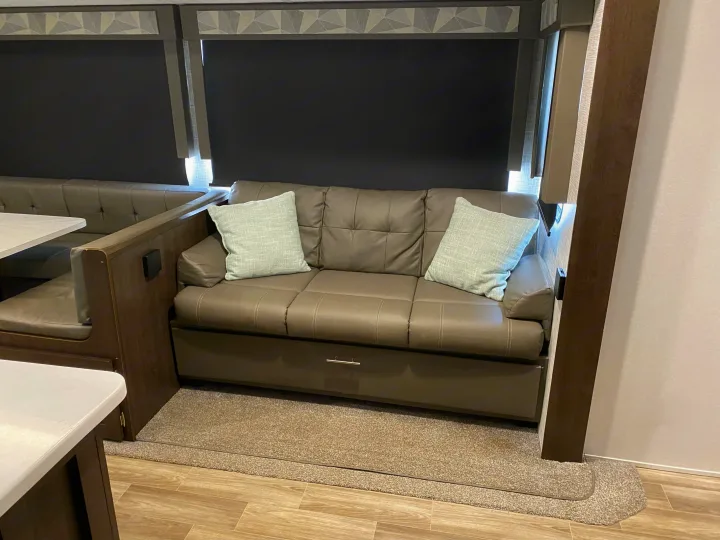 RV rental living space featuring a comfortable sofa with pillows, dinette, and large windows with privacy blinds.. Forest River Wildwood 2020