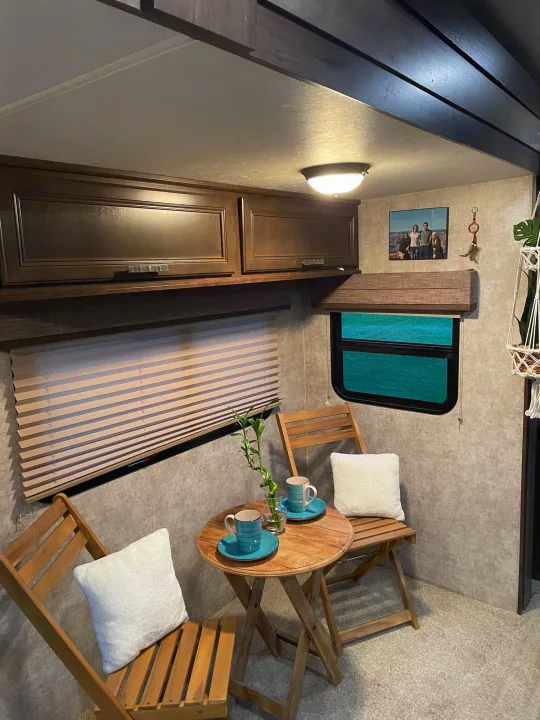 Cozy RV rental interior features a small dining table with two chairs, cups, a plant, and overhead cabinets.. Highland Open Range 2017