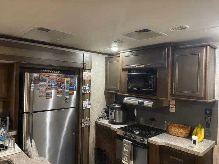 Discover a functional RV rental kitchen with stainless steel fridge, microwave, and gas stove, ready for your travel adventures.. Highland Open Range 2017