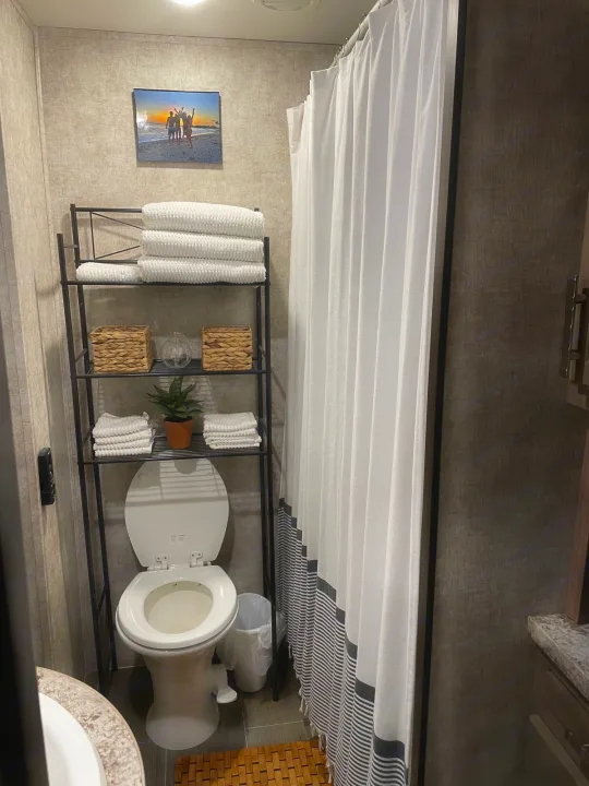 RV rental bathroom features organized over-toilet shelving with white towels, decor, and a white/striped shower.. Highland Open Range 2017