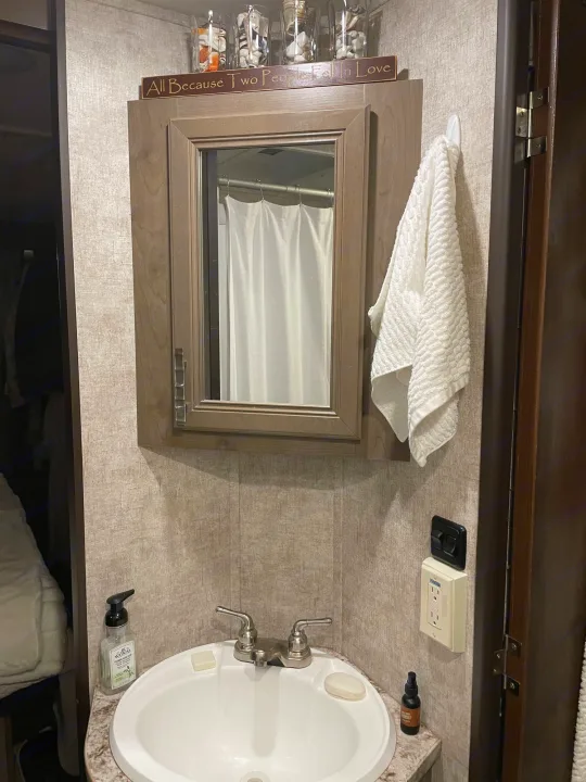 RV rental bathroom with sink, mirror, towel, and "All Because Two People Fell in Love" sign. Compact & functional.. Highland Open Range 2017