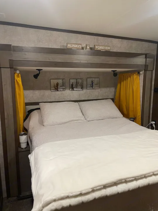 Cozy RV rental bedroom interior featuring a comfortable bed, personal photos, and yellow curtains. Perfect for your next trip!. Highland Open Range 2017