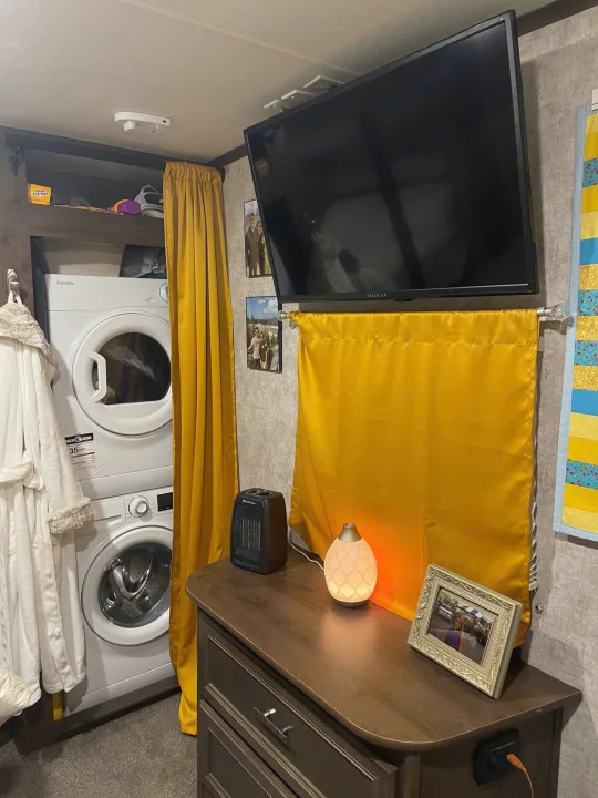 Cozy RV rental interior with stacked washer/dryer, wall-mounted TV, dresser, and decor.. Highland Open Range 2017