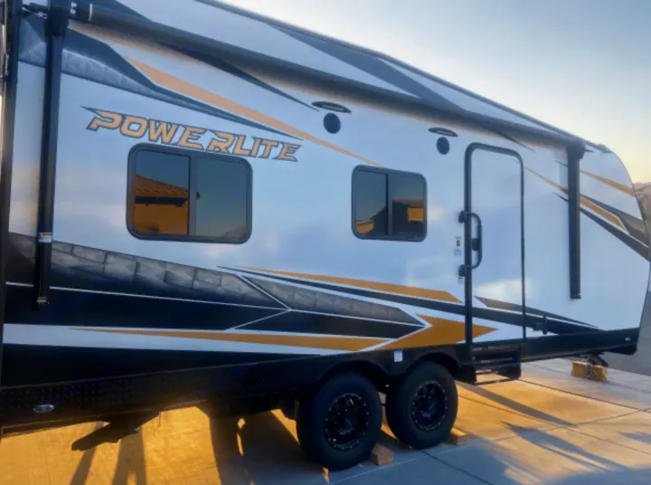 Side view of a white, gold, and black Powerlite travel trailer, ready for an RV rental getaway.. Genesis Supreme Rv Powerlite Prime 1915 2022