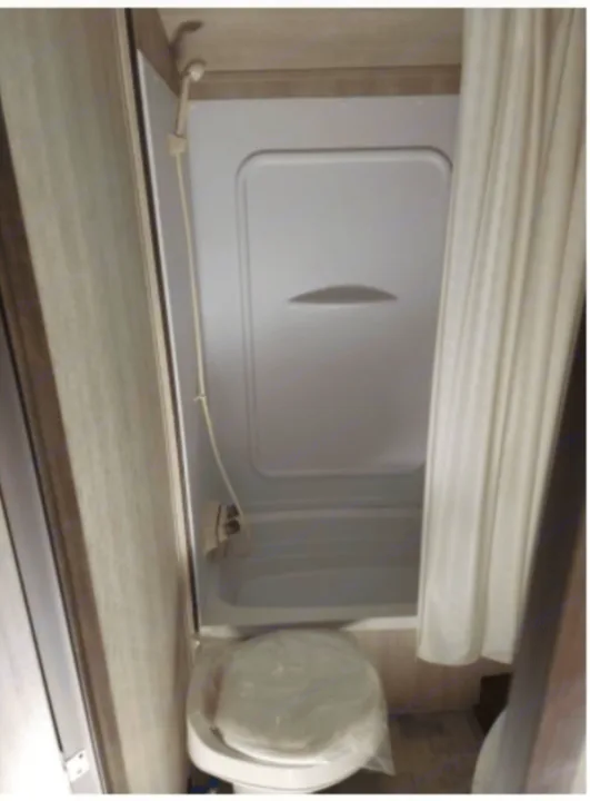 This RV rental features a compact bathroom with a white shower, handheld showerhead, and a covered toilet, ideal for travel.. Genesis Supreme Rv Powerlite Prime 1915 2022