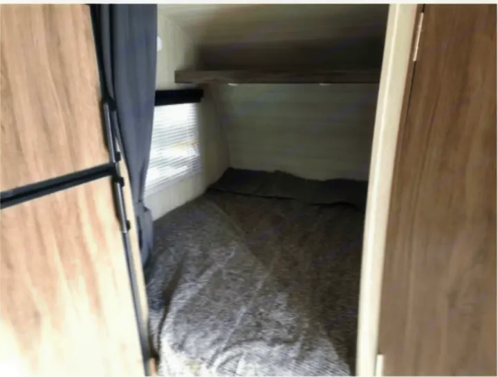 RV rental bedroom interior: A cozy bed with gray bedding, a small window, and an overhead shelf. Compact RV living space.. Genesis Supreme Rv Powerlite Prime 1915 2022