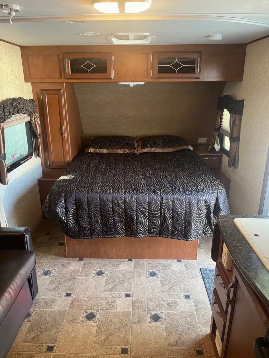 This RV rental offers a compact and comfortable bedroom with a queen bed, decorative quilt, and ample storage.. Winnebago Other 2013