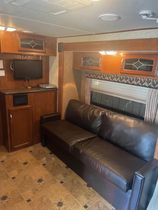 Comfortable RV rental interior with a dark leather-look sofa, entertainment center, and overhead storage cabinets.. Winnebago Other 2013