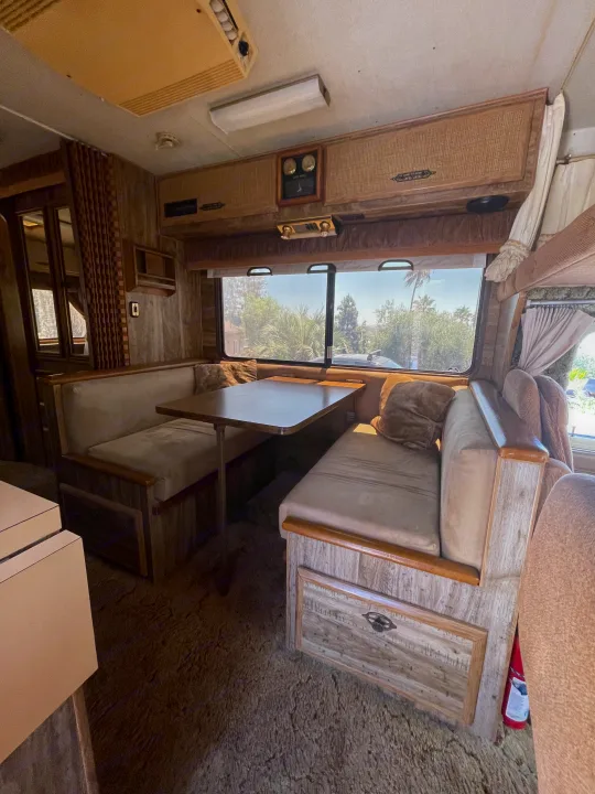 Inside a vintage RV rental: dinette seating, wood cabinets, and large windows offer a comfy travel space.. Chevrolet Lazy Daze 1985